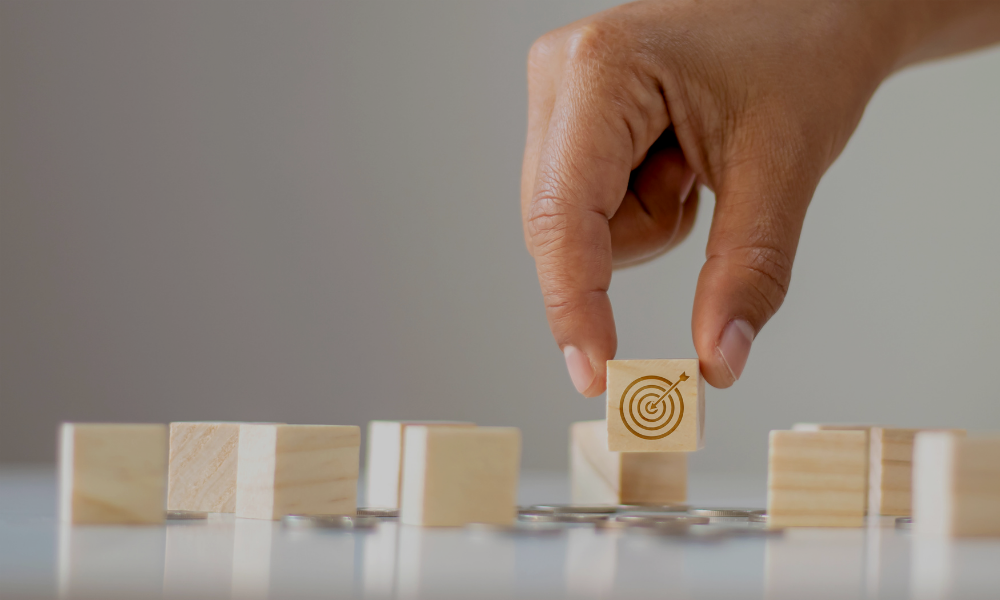 a person's hand picking up a small wooden block with a target on it